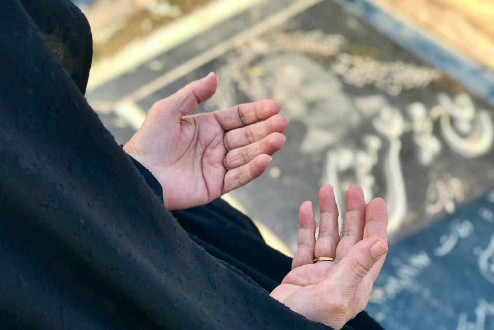 Kvinna klädd i svart håller upp sina händer i traditionell islamsk bön vid en grav